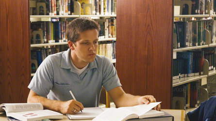 A student writing at a desk in a library